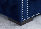 Close-up of a blue velvet sofa with nailhead trim on a gray floor.