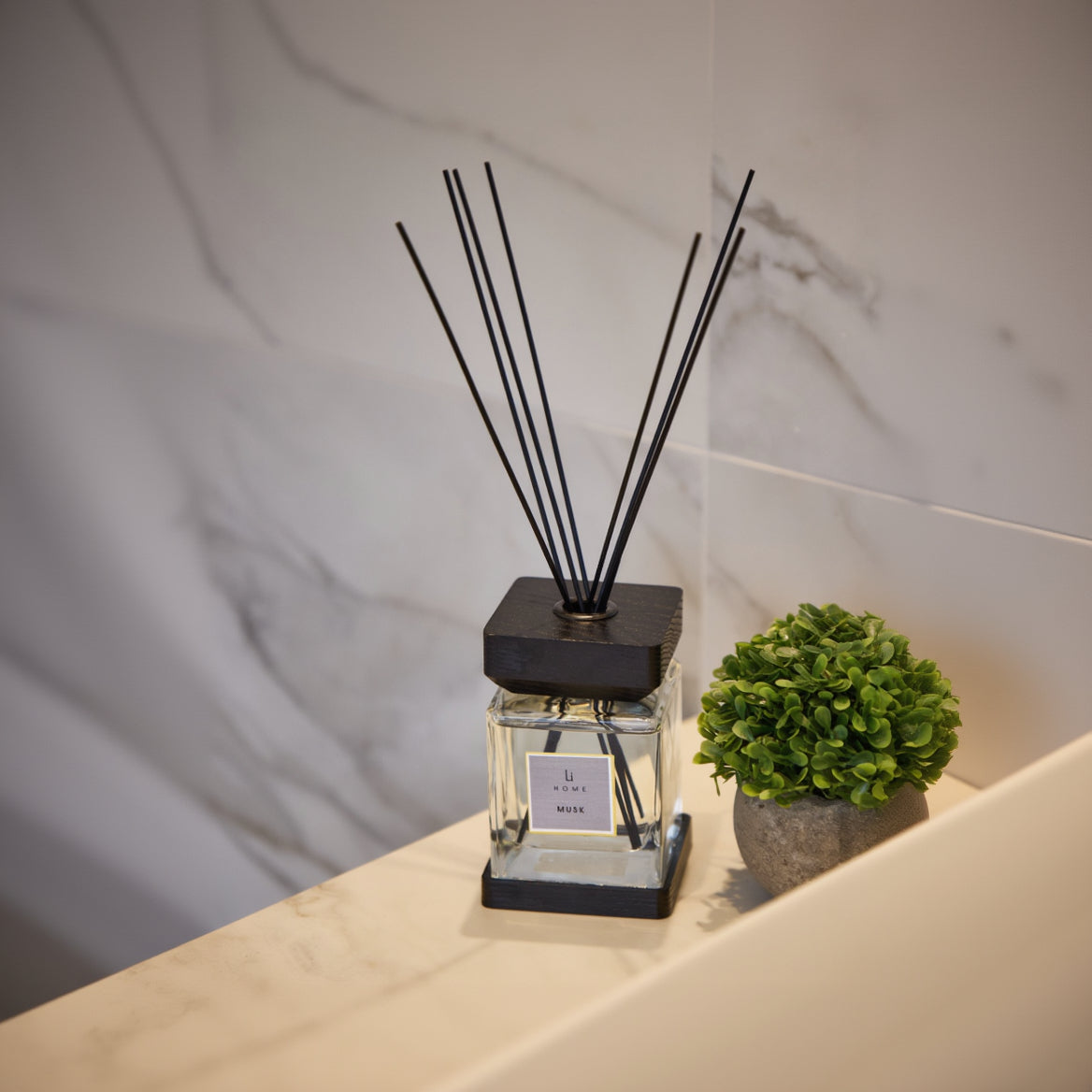 A diffuser with black sticks on a marble surface with a plant in the background