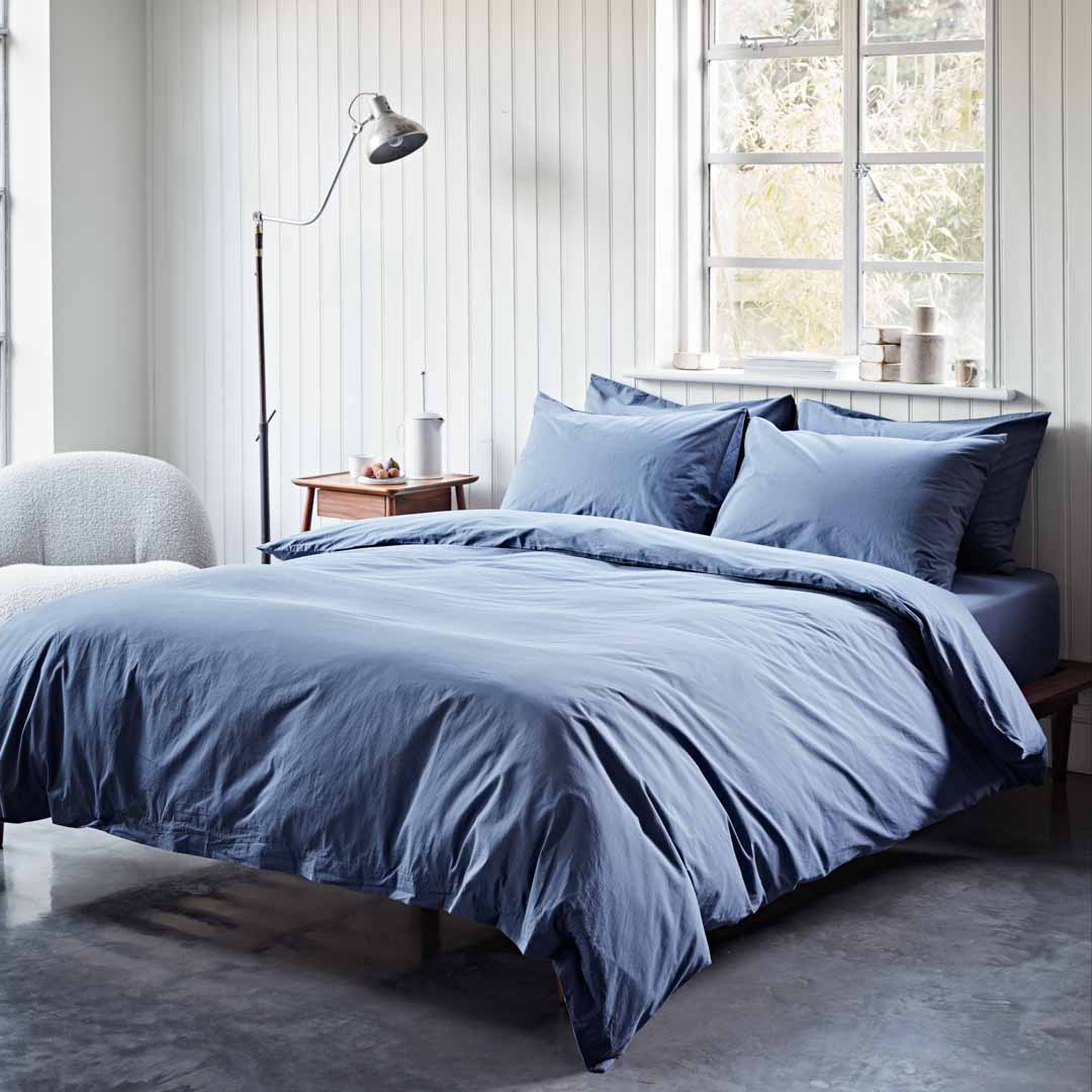 Blue bedding set on a bed in a bright bedroom with large windows.