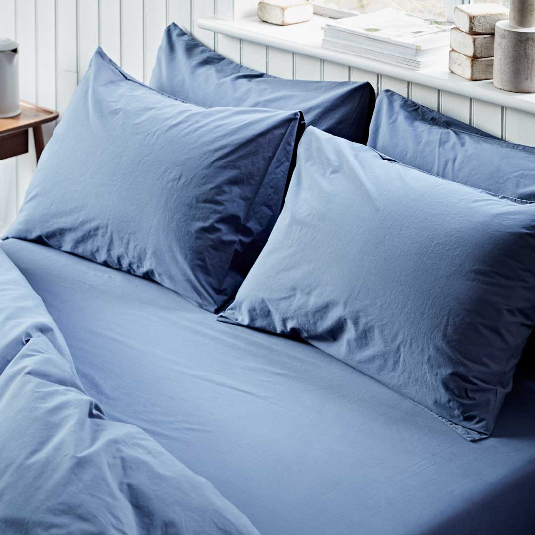 Blue bedding set with pillows on a bed in a bedroom setting.