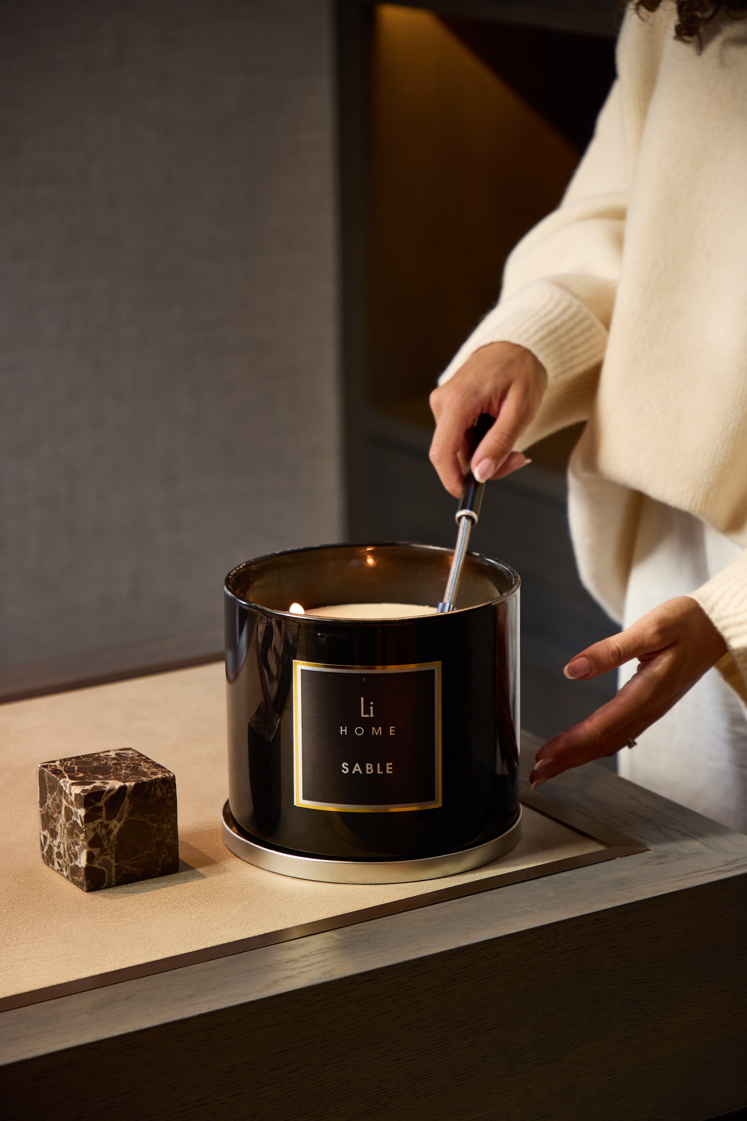 Person lighting a candle labeled 'Sable' from Li Bien on a wooden surface.