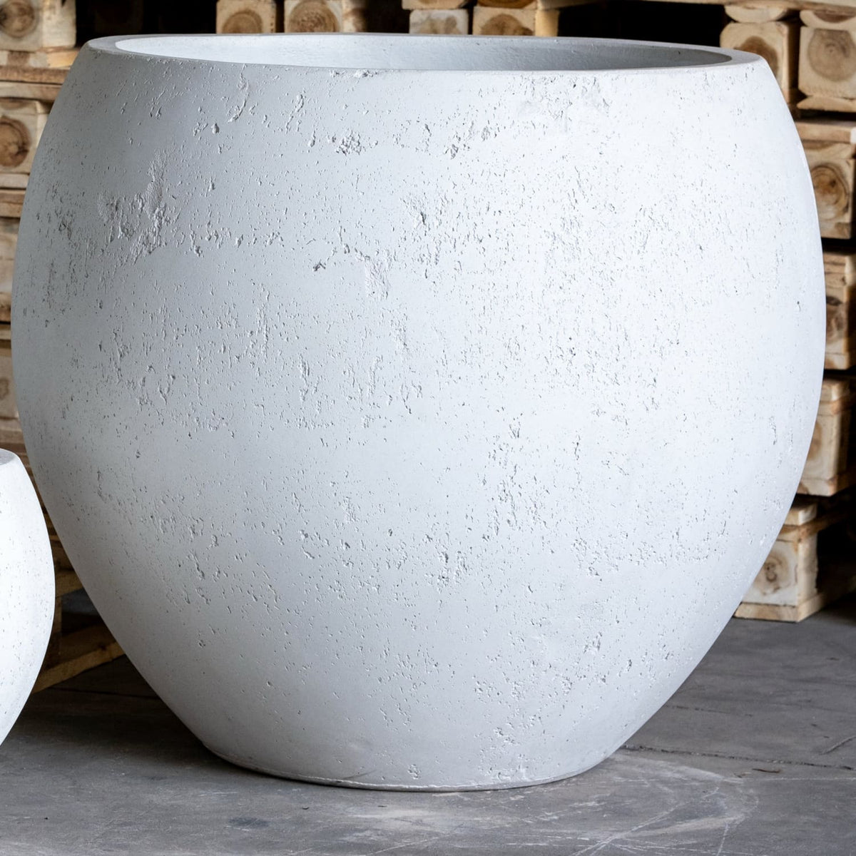 Large white concrete planter in front of wooden pallets