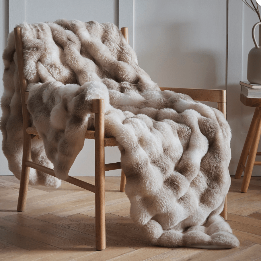 Beige fluffy blanket draped over a wooden chair in a room with a neutral color scheme.