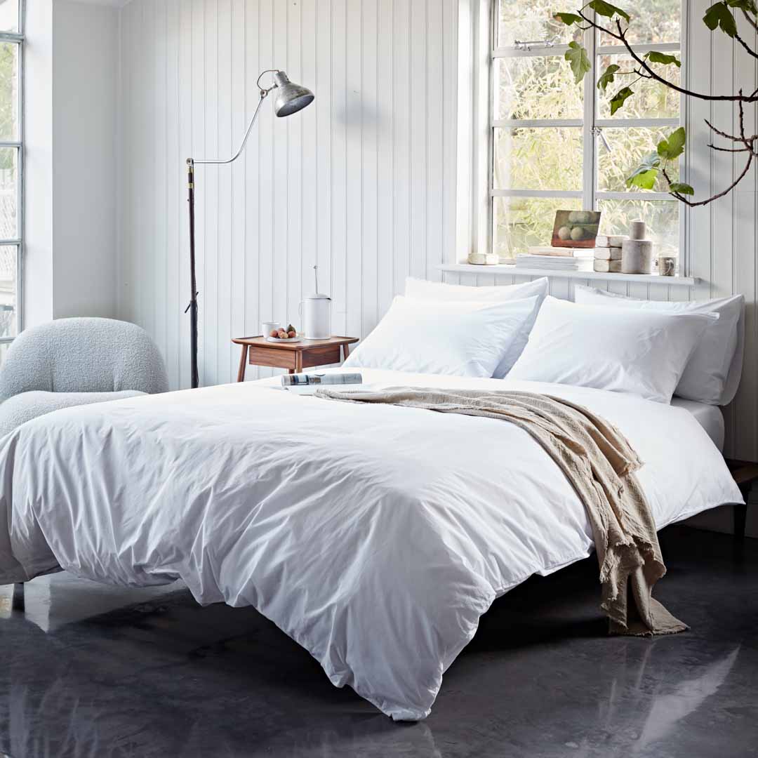 Neatly made bed with white bedding in a bright bedroom.