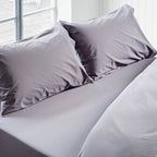 Gray bedding set with pillows on a bed in a bright room.