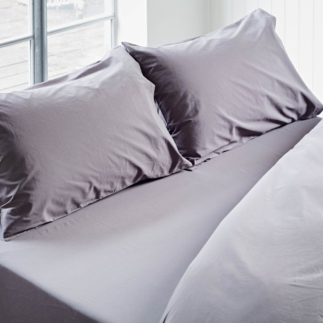 Gray bedding set with pillows on a bed in a bright room.