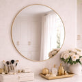 Round gold-framed mirror on a white wall with decorative items below.