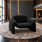 Modern sculptural armchair in dark charcoal bouclé fabric on a round textured rug in a luxury contemporary interior with warm ambient lighting.