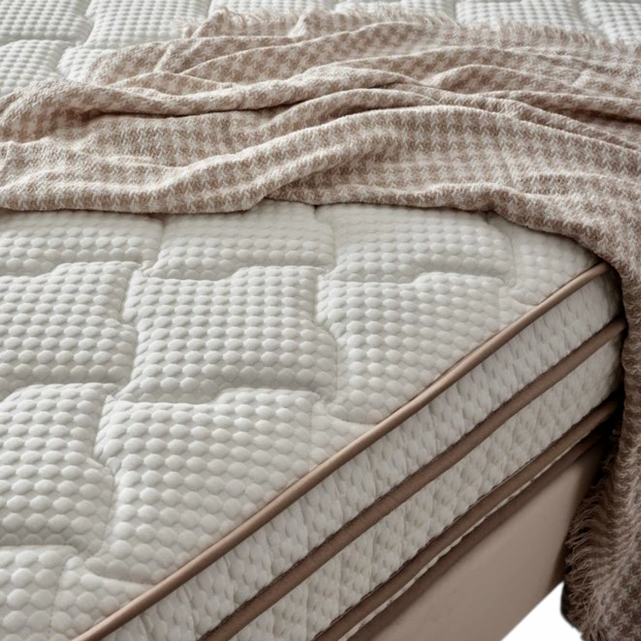 A close-up of a quilted mattress with a textured cream-colored cover, styled with a beige and white patterned throw blanket draped across the top.