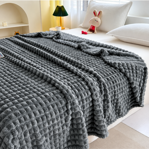 A thick, textured gray blanket with a chunky bubble pattern draped over a bed in a bright, modern bedroom setting.