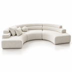 Modern curved modular sectional sofa in light warm off-white fabric on a clean white studio background, with matching throw pillows and a round cushion.