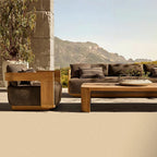 Modern outdoor patio furniture set with a wooden armchair, matching coffee table, and a dark brown sectional sofa, styled on a concrete patio with a stone column and mountain backdrop.