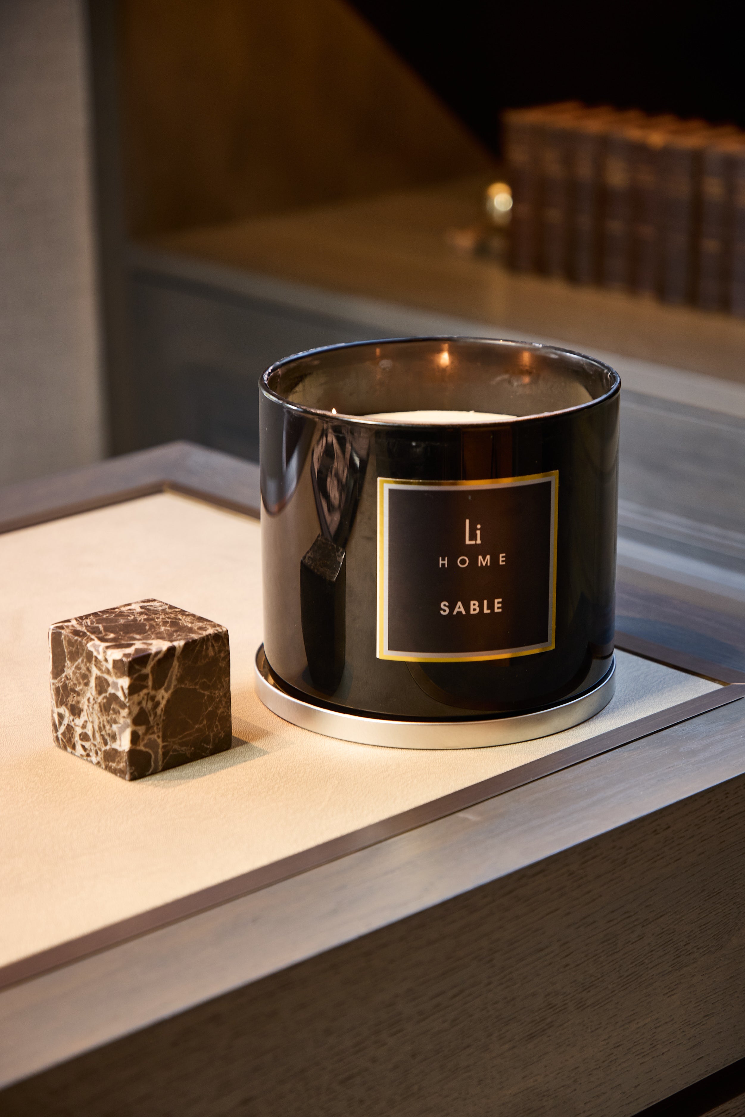 Black candle labeled 'Home Sable' on a reflective surface with a blurred background