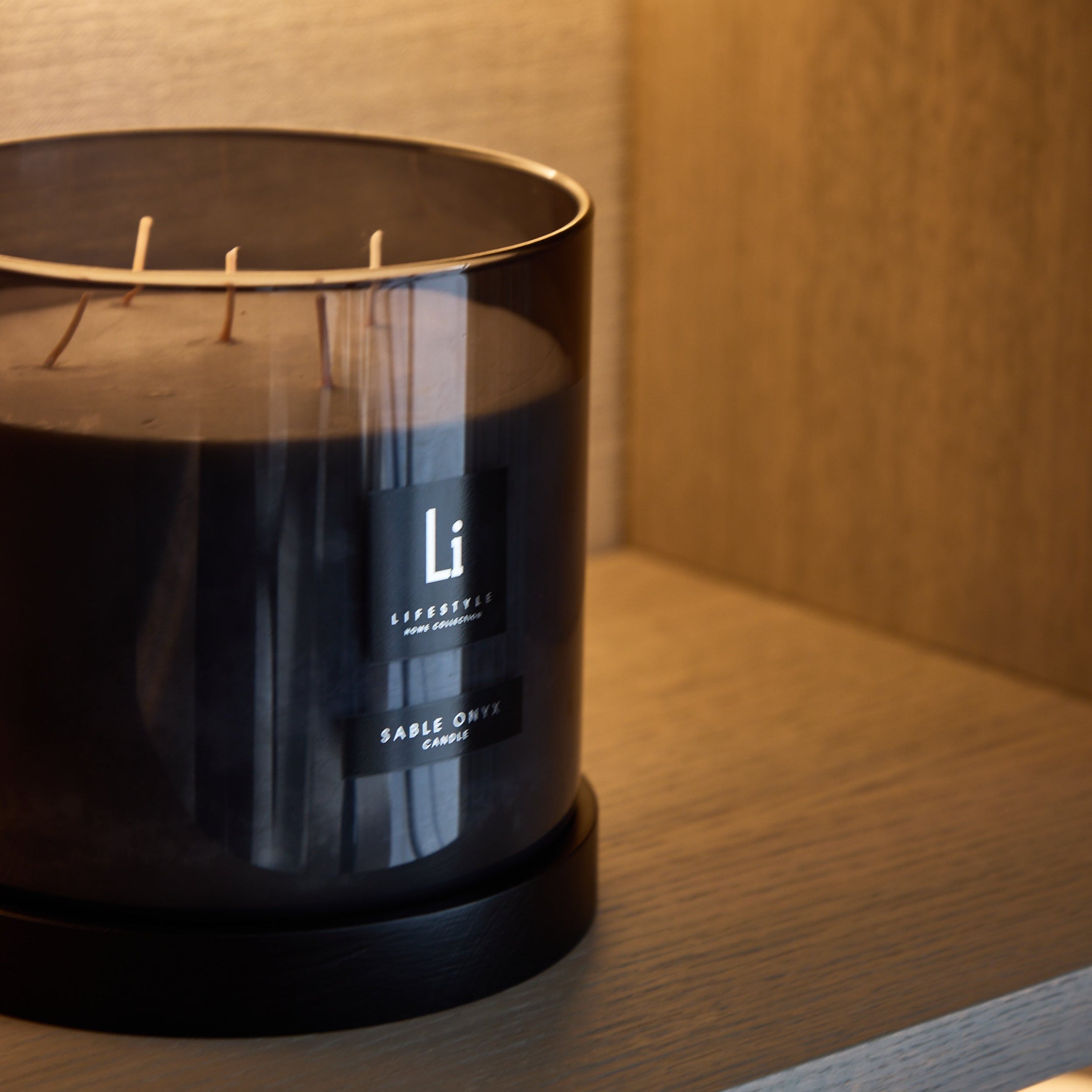 Black candle with 'Li' branding on a wooden shelf