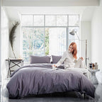 Woman sitting on a bed with gray bedding in a bright bedroom