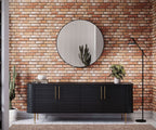 Black cabinet with gold handles against a brick wallpaper with a round mirror above it.