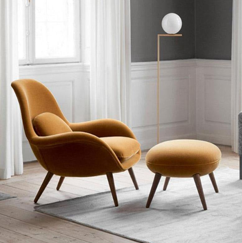 Mustard yellow armchair and ottoman with a floor lamp in a room with large windows.