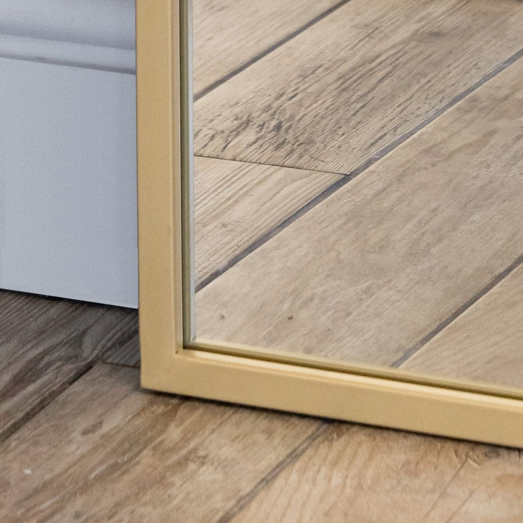 Close-up of a wooden floor with a gold-framed mirror reflecting the room.