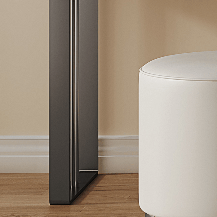 Black refrigerator against a beige wall with a white ottoman on a wooden floor.