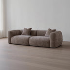 Brown sofa with two cushions on a wooden floor against a white wall