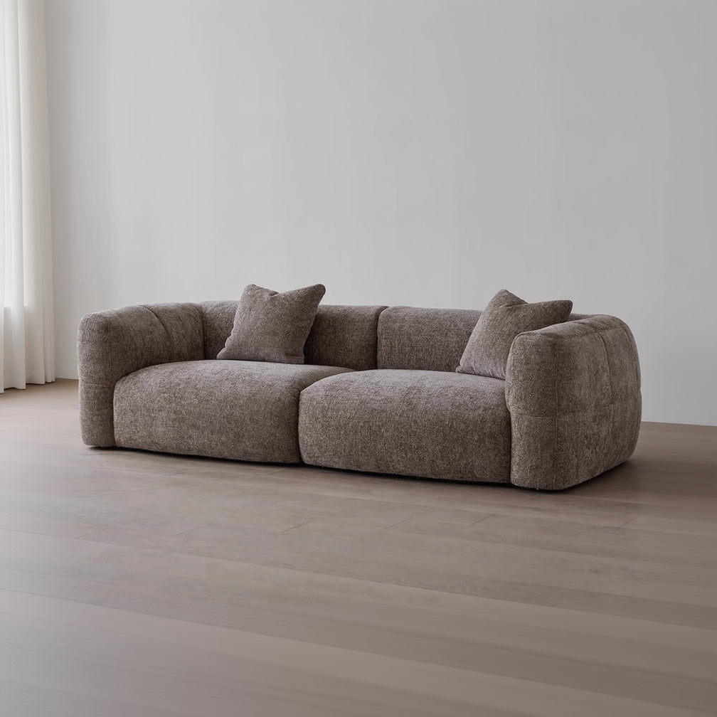 Brown sofa with two cushions on a wooden floor against a white wall