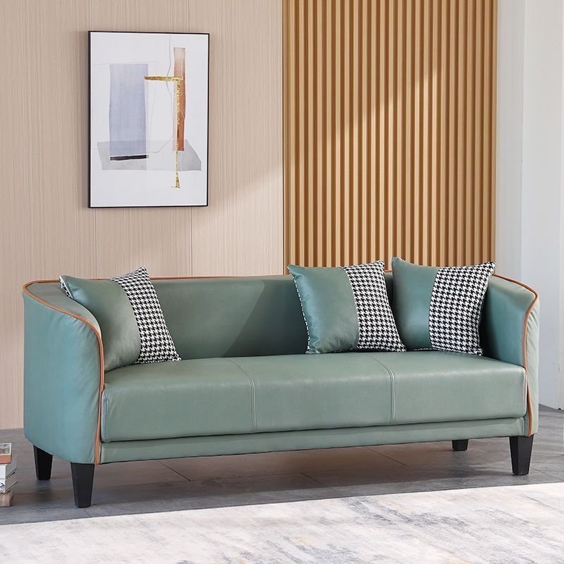 Green sofa with decorative pillows in a room with a wooden wall and framed picture.