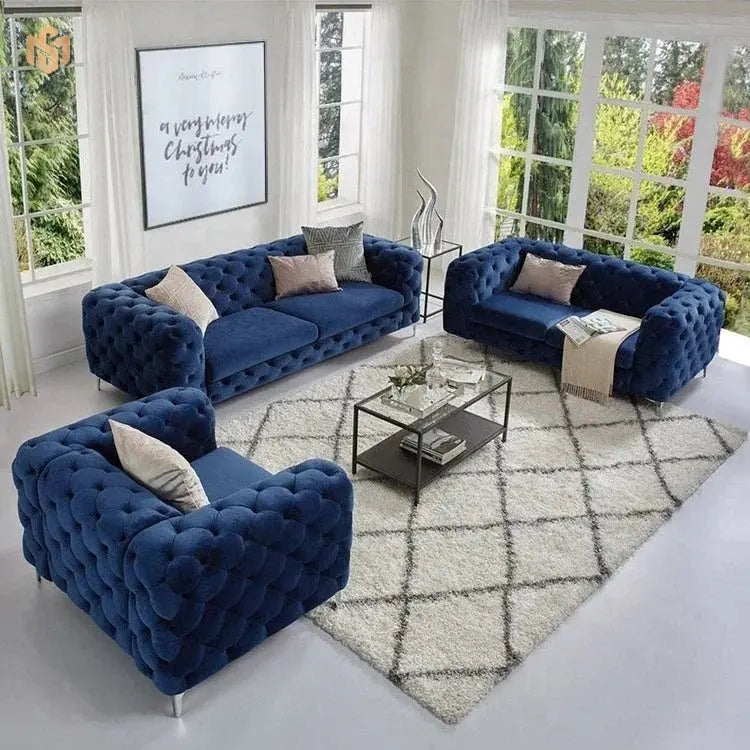 Blue velvet sofa set in a modern living room with a geometric rug and glass coffee table.