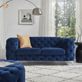 Blue tufted sofa in a living room with a plaid pillow and large window.
