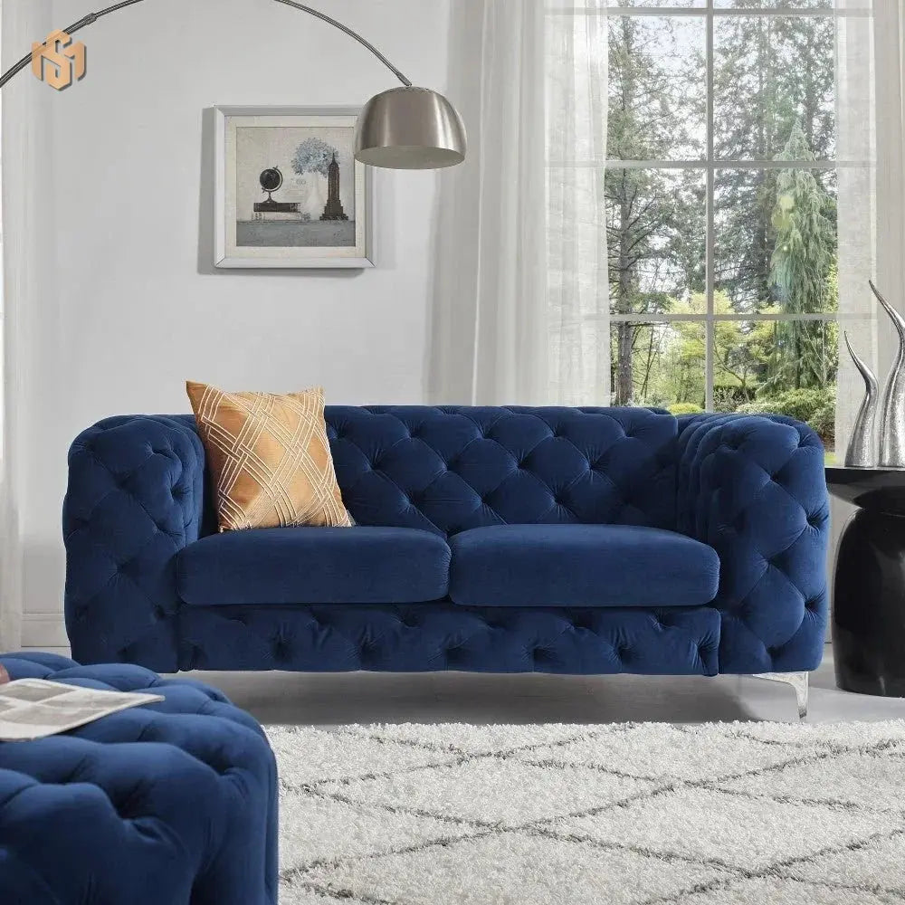 Blue tufted sofa in a living room with a plaid pillow and large window.