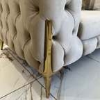 Beige tufted sofa with gold legs on a marble floor