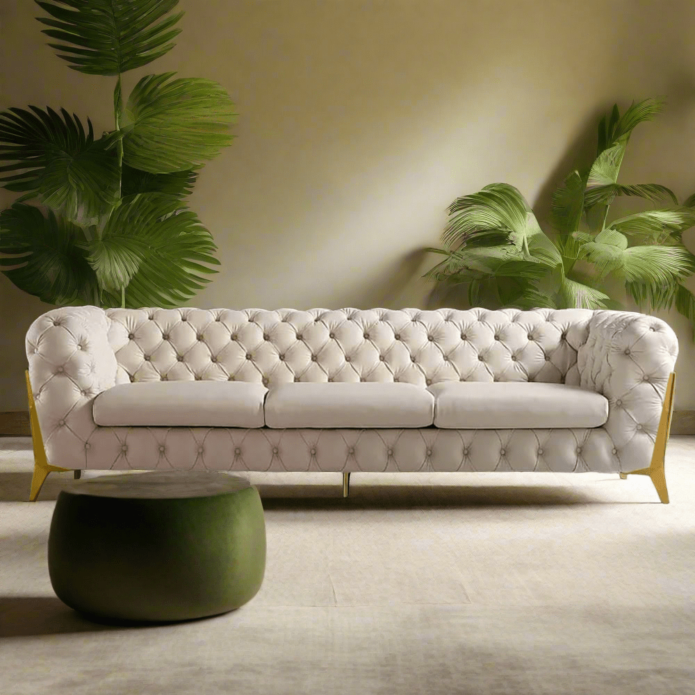 White tufted sofa with gold legs in a room with plants and a green side table.