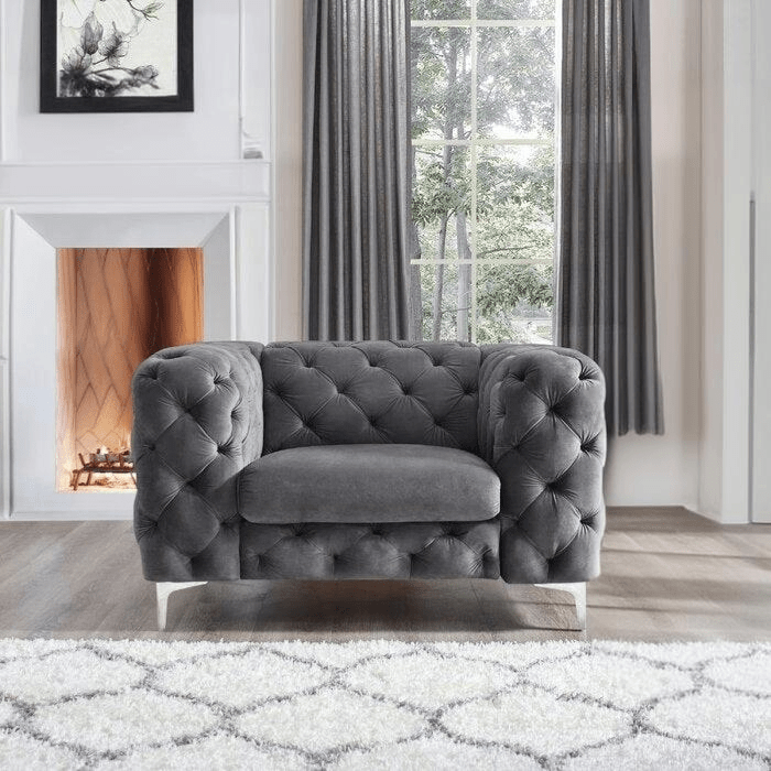 Gray tufted armchair in a living room with a fireplace and large window.