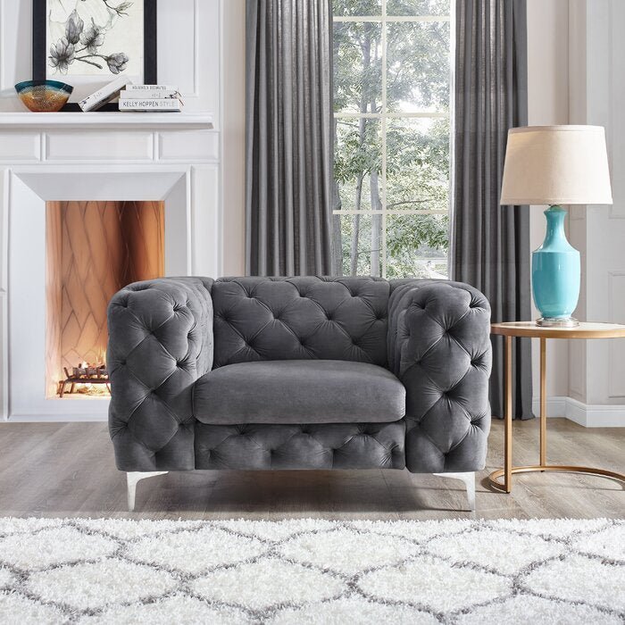 Gray tufted armchair in a living room with a fireplace and large window.