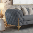 Gray tufted sofa with wooden legs against a marble wall.