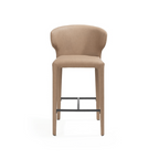 A modern barstool with a curved backrest and seat upholstered in a warm beige fabric, supported by slim wooden legs and a black metal footrest, shown against a plain white background.