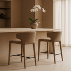Two beige bar stools in front of a light-colored counter with a vase of white flowers on a neutral background.