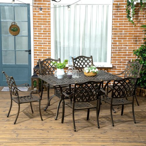 Outdoor patio set with table and chairs on a wooden deck against a brick wall.