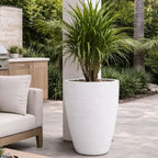 White planter with a green plant on a patio with outdoor furniture