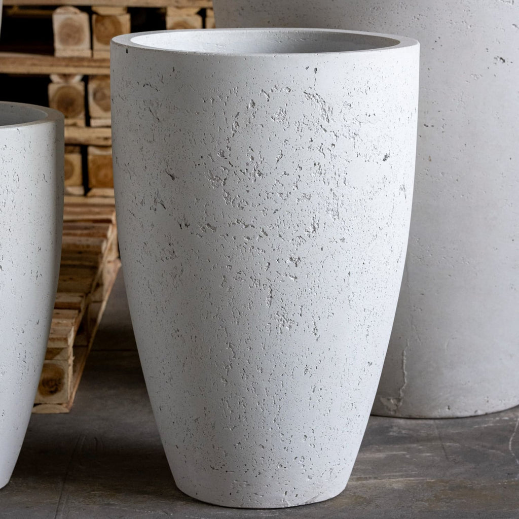 White concrete planters on a gray floor with wooden pallets in the background