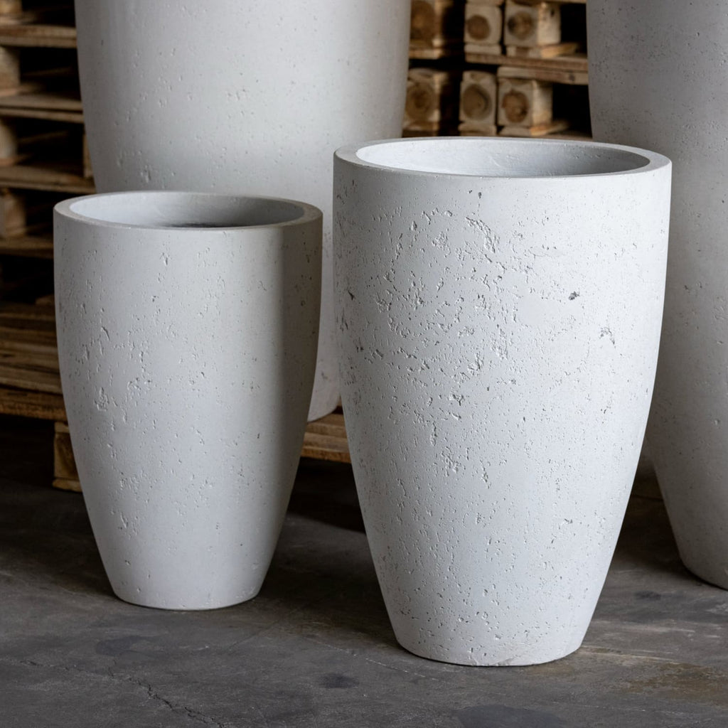Three large white concrete planters on a dark floor with wooden pallets in the background.