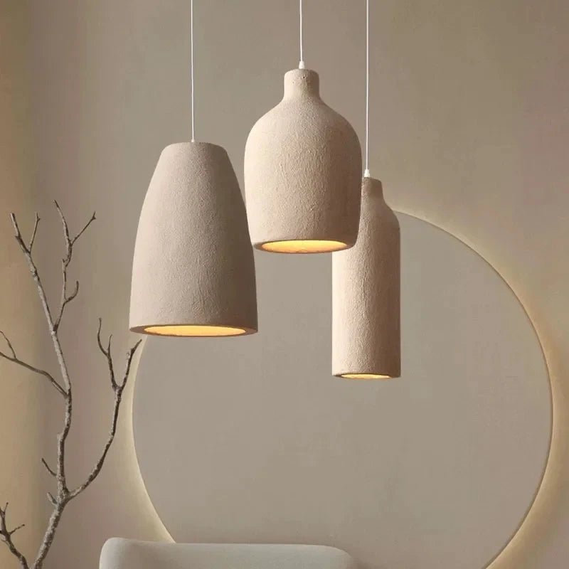 Three beige pendant lights hanging against a neutral wall with a branch on the left.