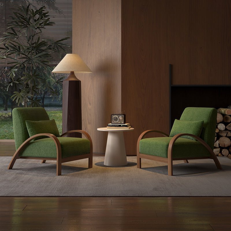 Two green armchairs with wooden frames in a room with a fireplace and lamp.